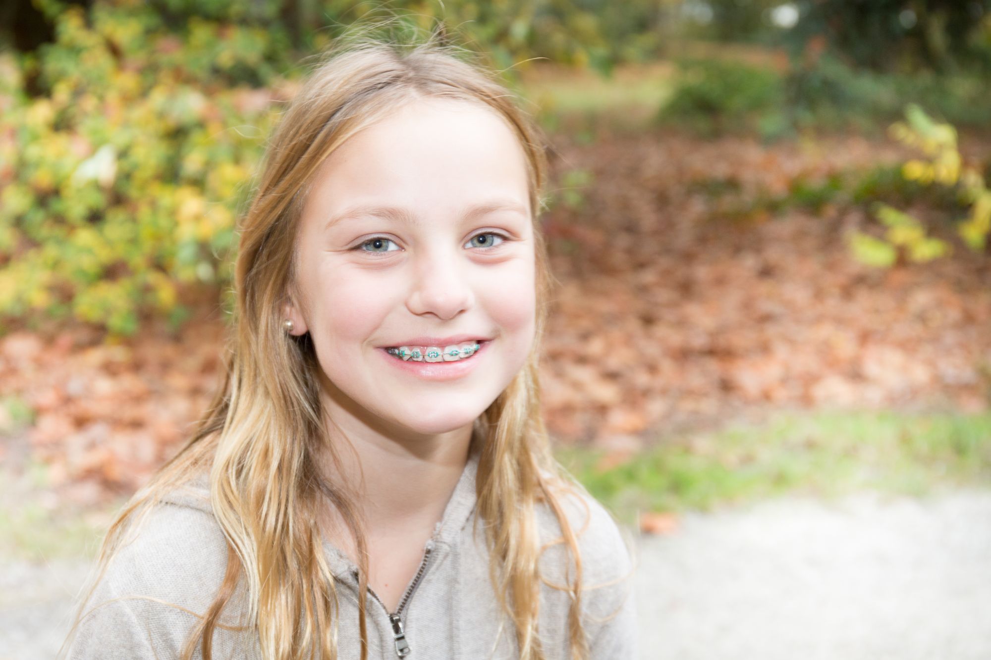 Smiling young girl with long blonde hair and braces outdoors in autumn, a happy orthodontic patient at Smile Ranch Orthodontics in Kingwood, TX – Kingwood orthodontics